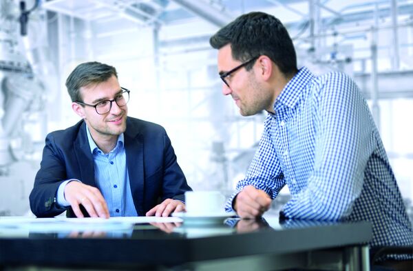 Zwei Männer im Gespräch an einem Tisch, besprechen Dokumente in einem modernen Büro