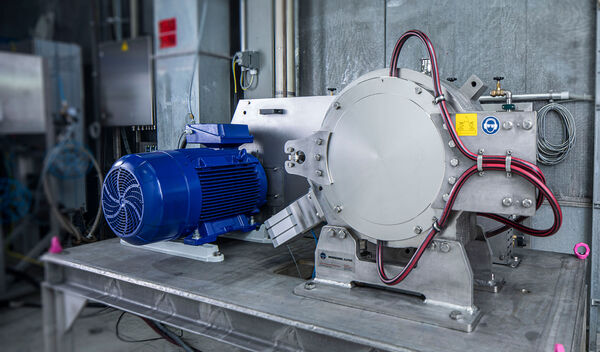Eine graue Hosokawa Sichtermühle namens Alpine Particle Rounder mit einem blauen Motor, die auf einem Metalltisch in einer Werkstatt steht