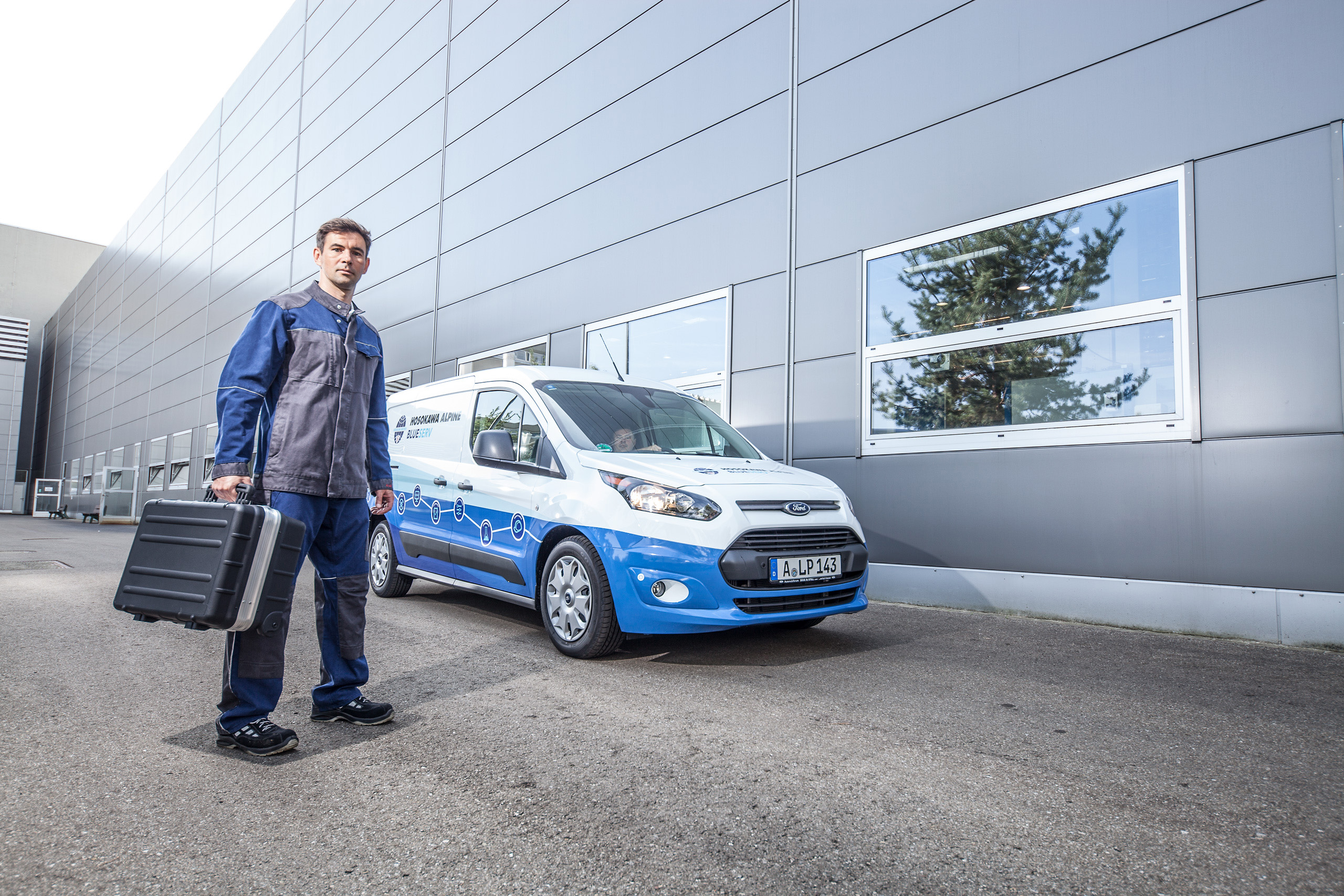 Blueserv Mitarbeiter mit Werkzeugkoffer vor gebrandeten Blueserv Auto
